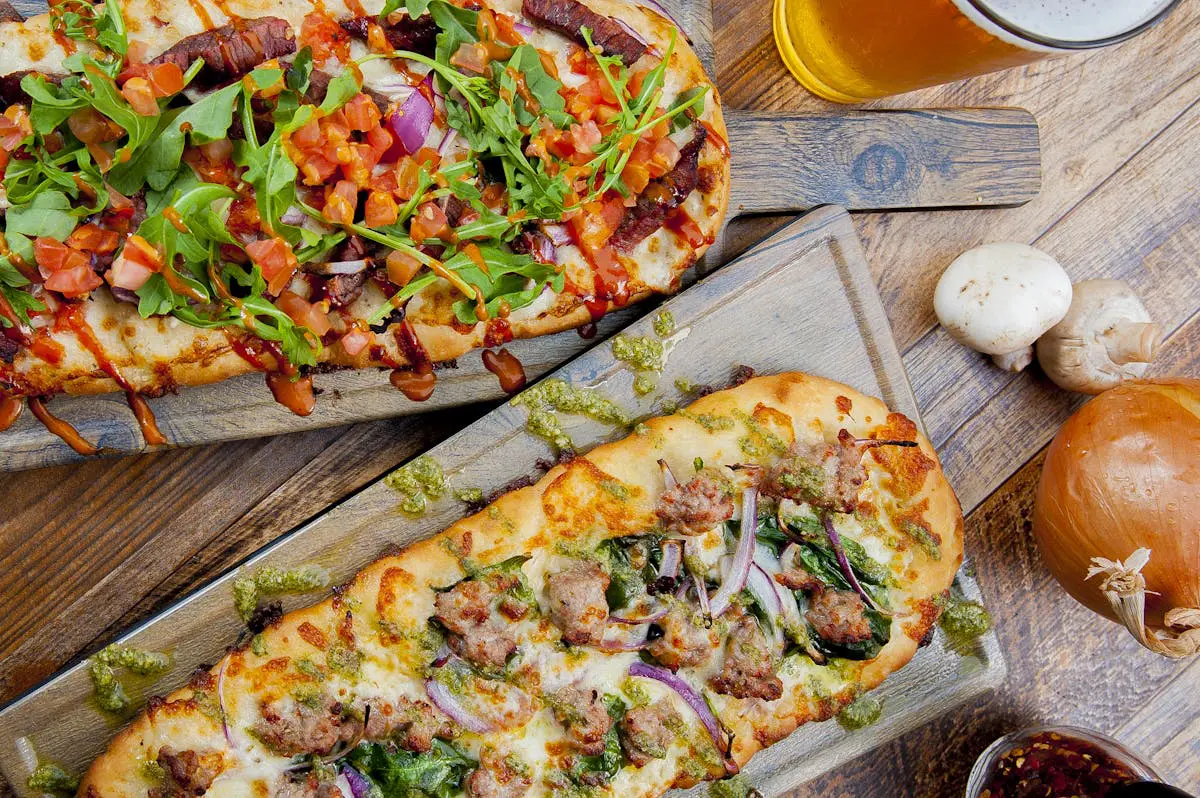 Two flatbread pizzas with various toppings on wooden boards.