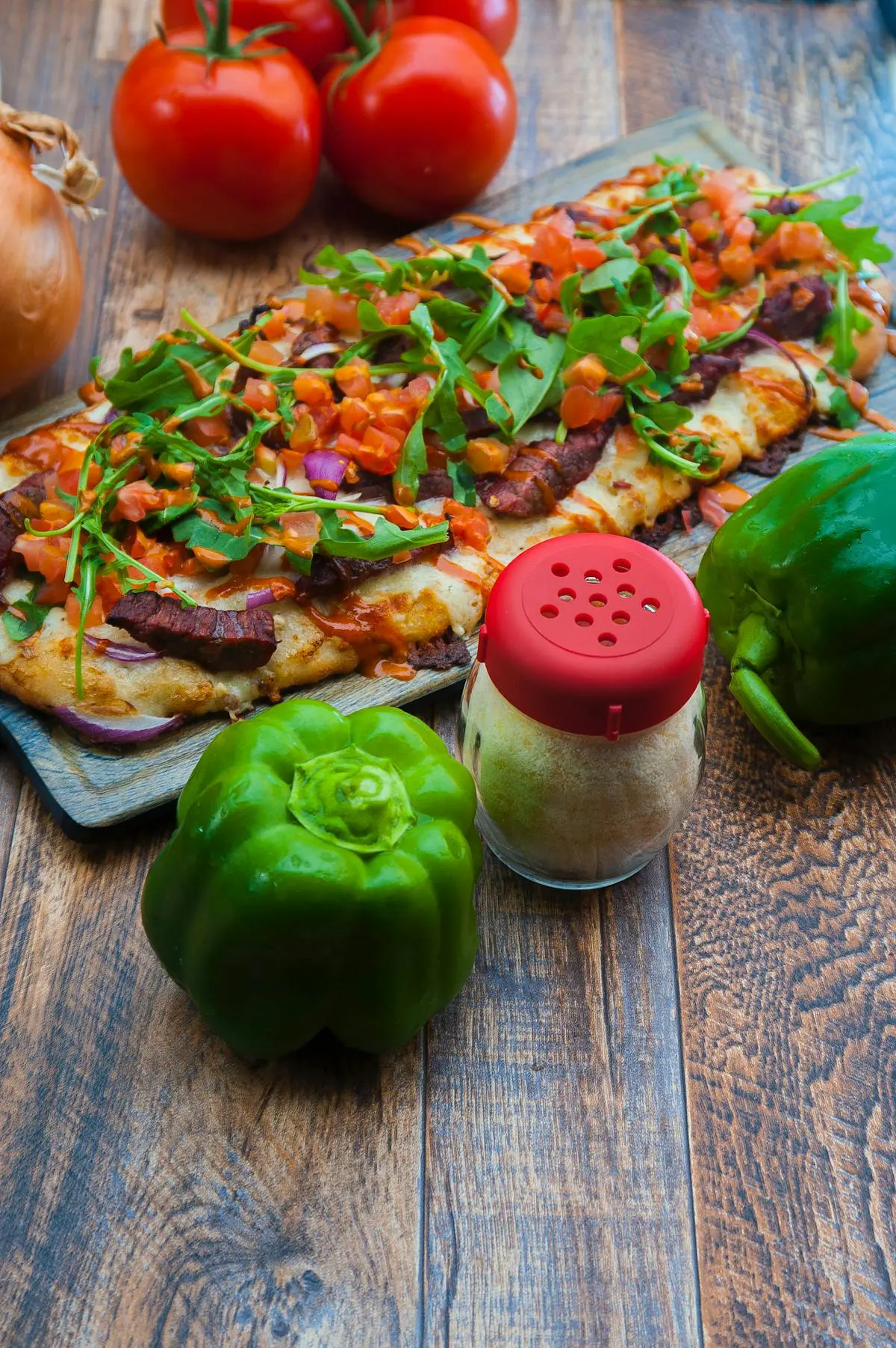 Fresh vegetable-topped flatbread pizza on wooden board with green bell peppers.
