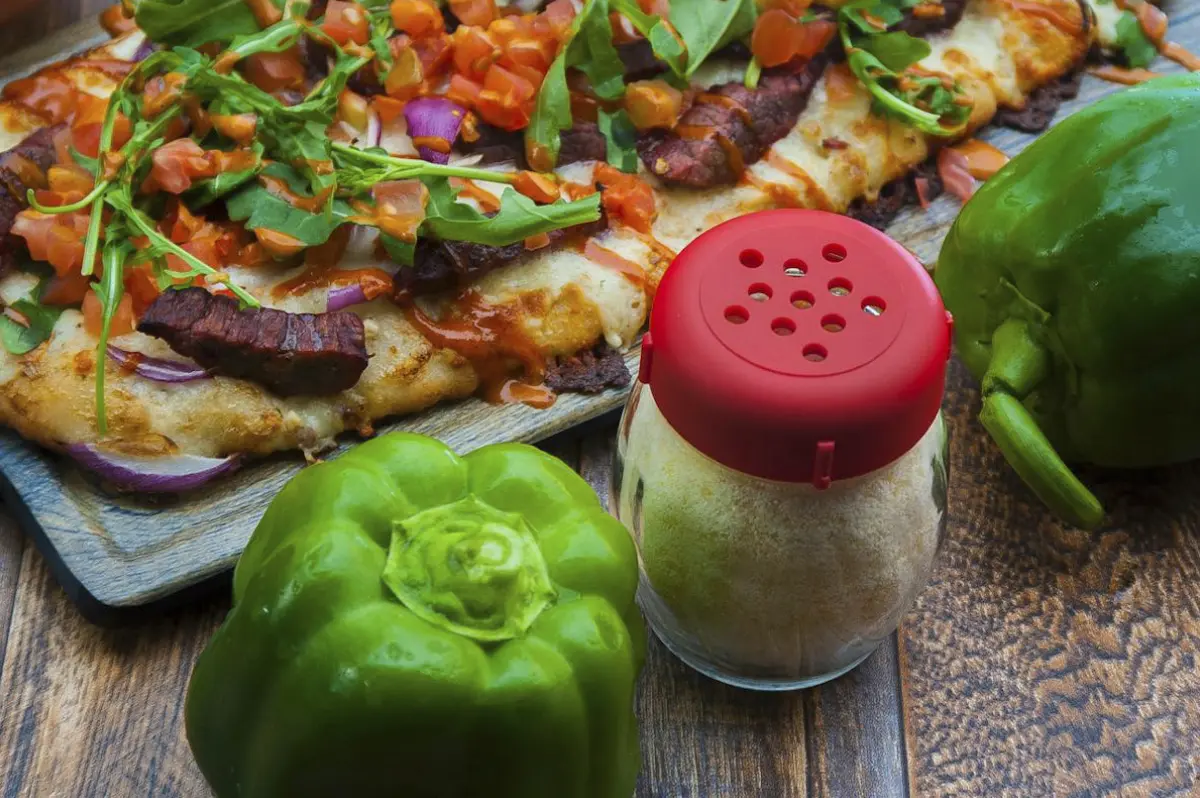 Green bell pepper and seasoning shaker on a wooden table.