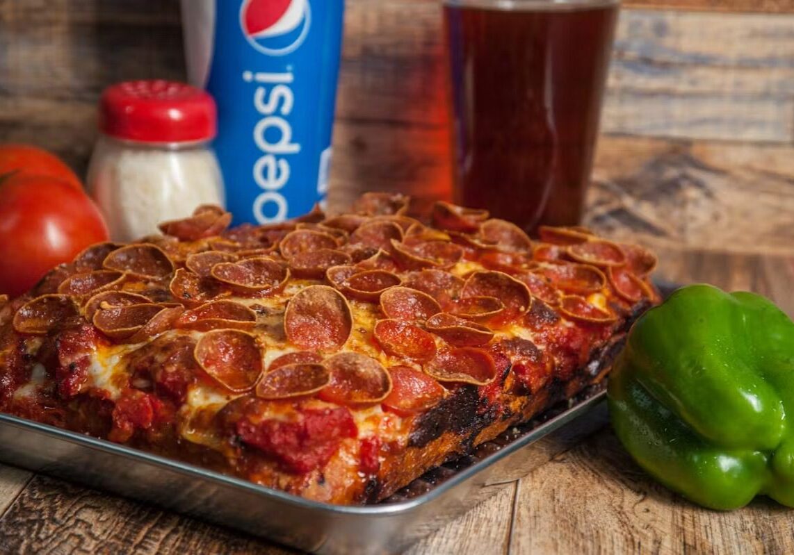 82669Deep_Dish A deep-dish pepperoni pizza with drinks in the background.