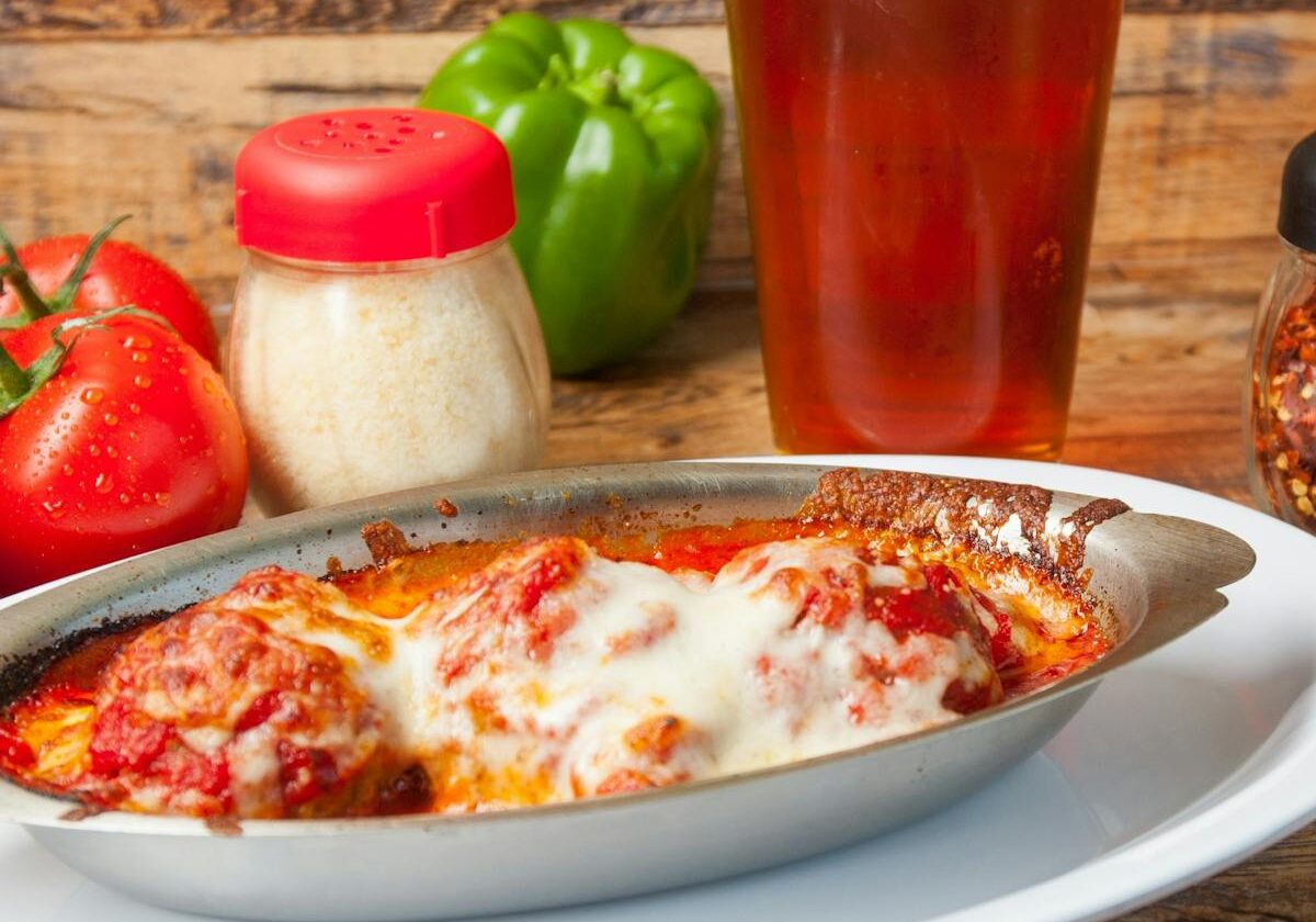asset 10 A plate of cheesy baked lasagna with a glass of beer in the background.
