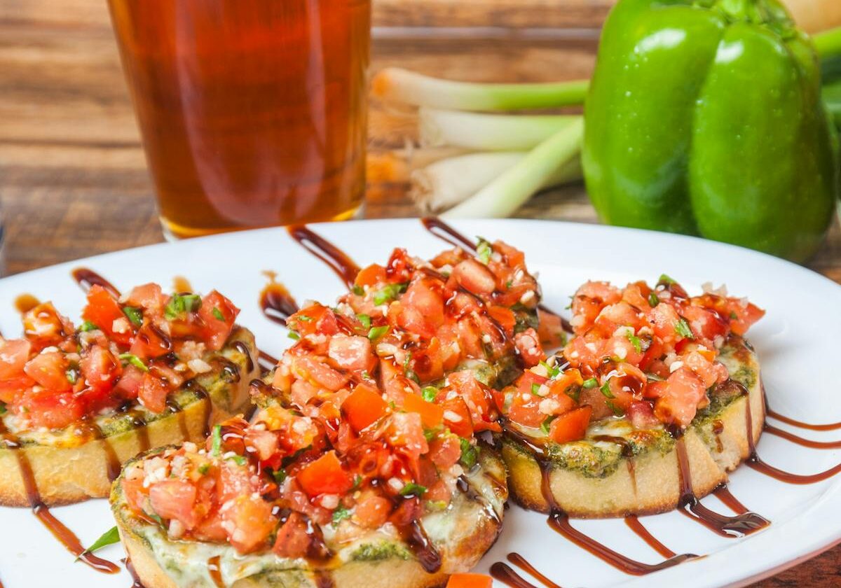 asset 11 A plate of bruschetta topped with diced tomatoes and herbs beside a glass of beer.
