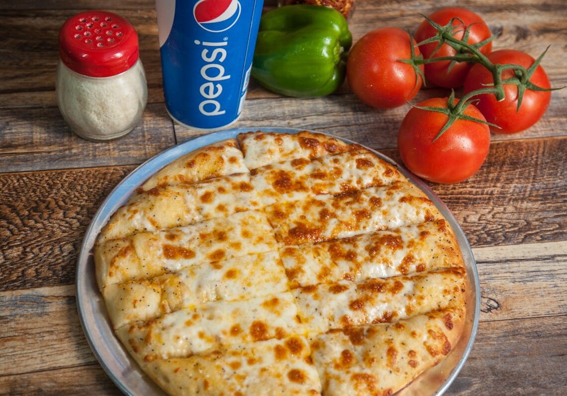 asset 20 A cheesy garlic bread on a plate with fresh vegetables and a Pepsi can in the background.