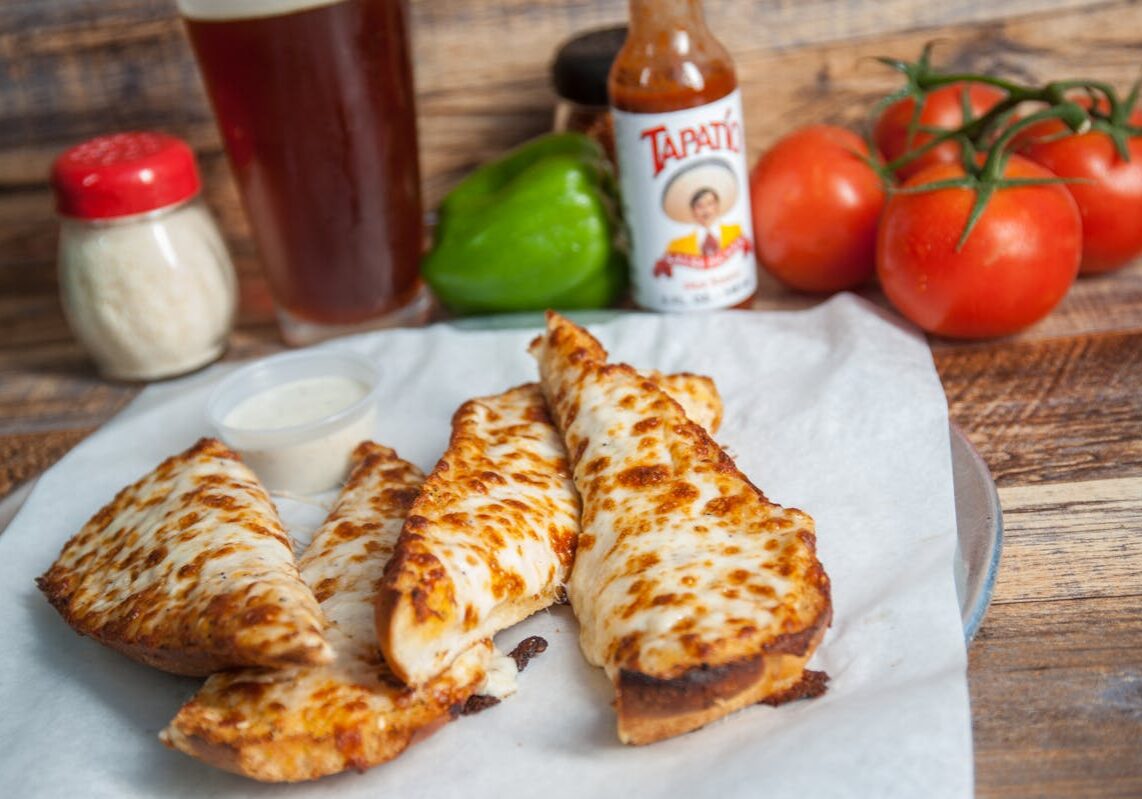 asset 21 Grilled chicken strips on parchment paper with fresh produce and hot sauce in the background.