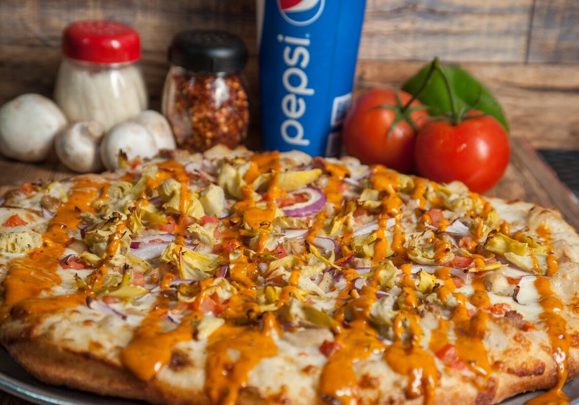 asset 31 A cheesy pizza drizzled with orange sauce and topped with chicken and onions.