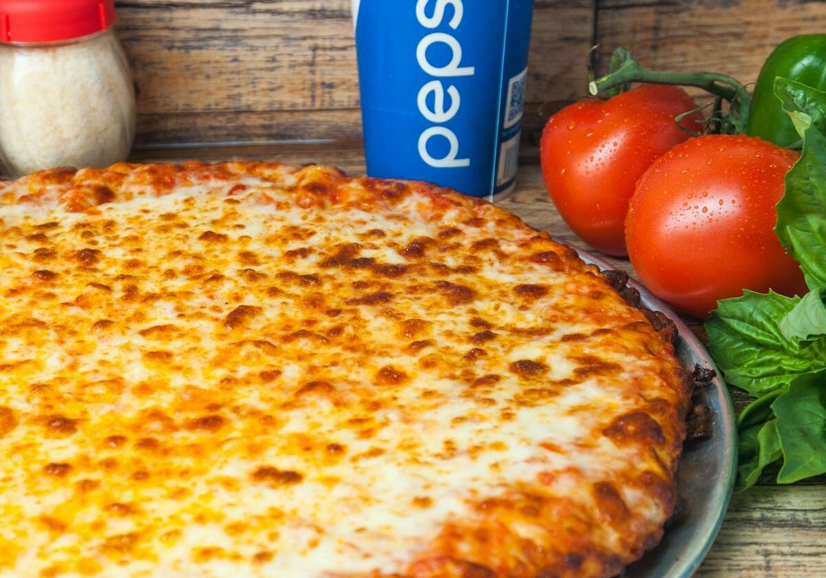 asset 37 A large cheese pizza with a Pepsi can and fresh vegetables.