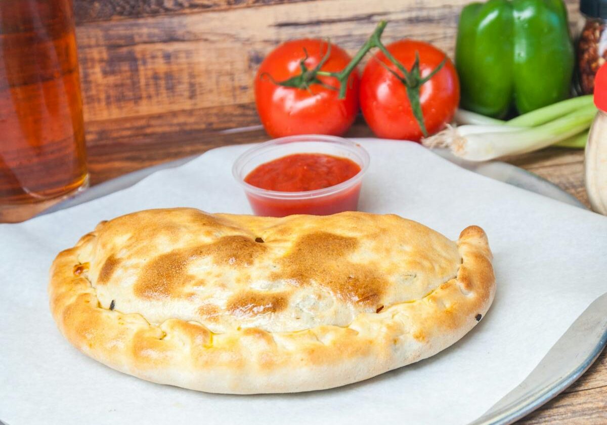 asset 43 A baked calzone on parchment paper with dipping sauce and vegetables.