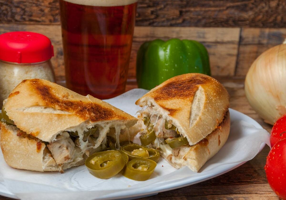 asset 47 A sandwich with melted cheese and jalapeños next to a glass of beer.
