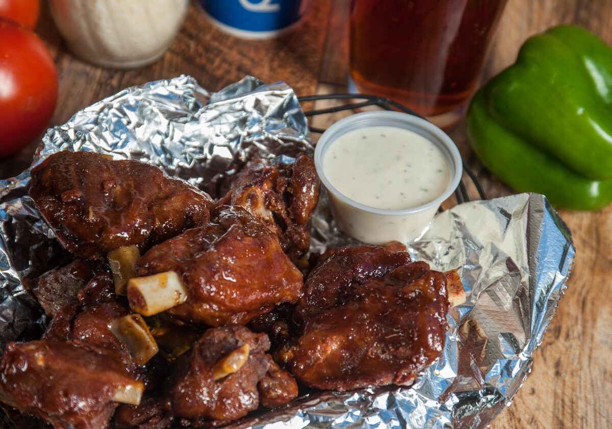 asset 5 Barbecue ribs with a cup of creamy dipping sauce on foil.
