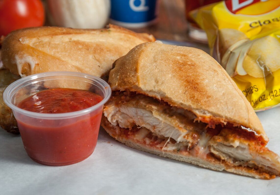 asset 54 A sandwich with fried chicken and a side of red sauce.