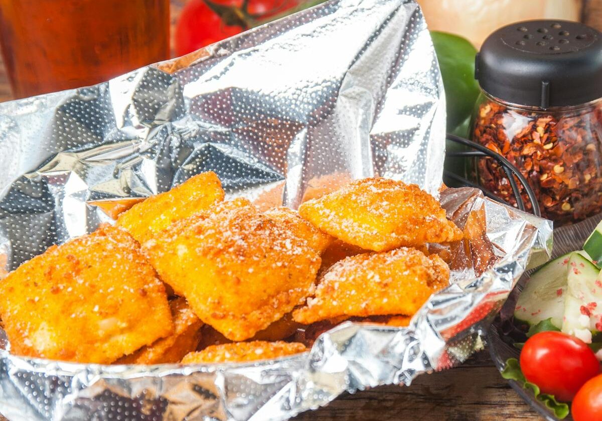 asset 6 Fried chicken pieces on foil with spices and vegetables.